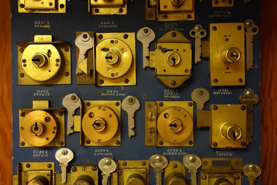 Dozens of brass drawer, cupboard and wardrobe locks mounted in rows on a blue display board, each with its key hung beside it and a small handwritten label beneath.
