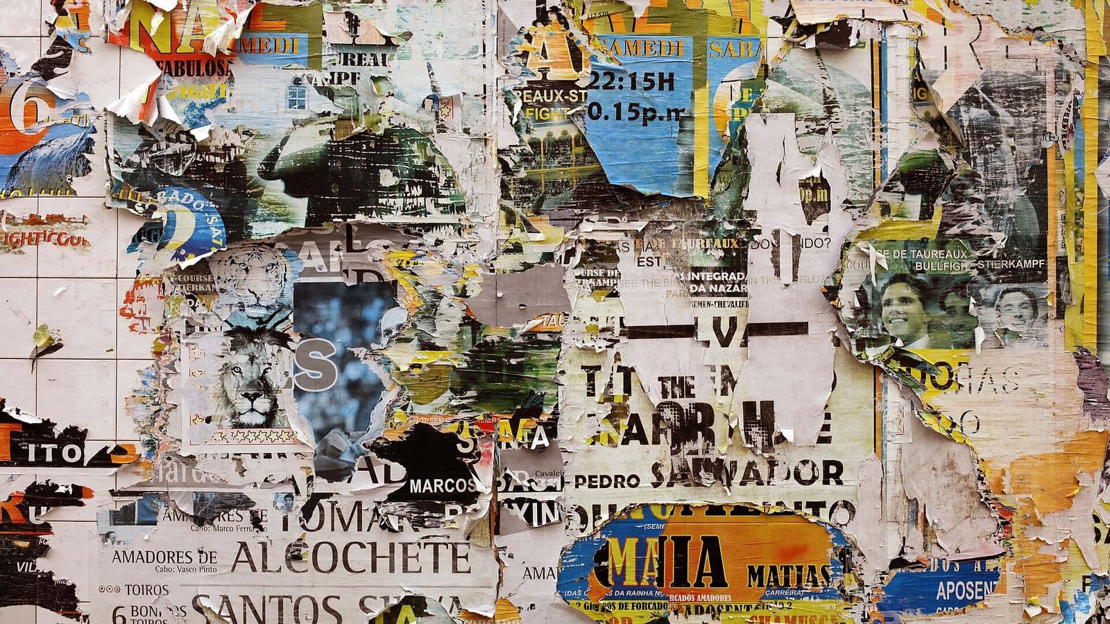 A wall covered in overlapping, peeling festival and bullfight posters in faded reds, yellows and blues.
