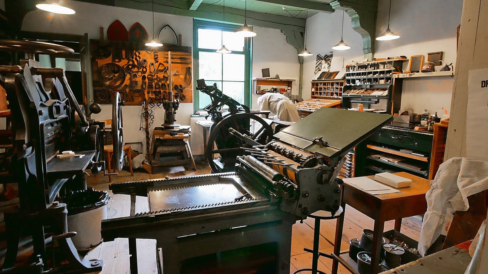 A reconstructed nineteenth-century printing workshop: a cast-iron cylinder press in the foreground, hand presses behind it and wooden type cases along the wall.